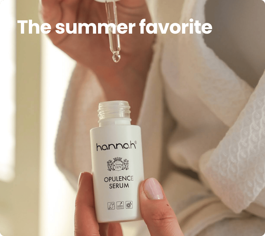 Een persoon in een witte badjas houdt een flesje hannah opulence serum vast terwijl er een druppel uit een pipet valt met de engelse tekst the summer favorite