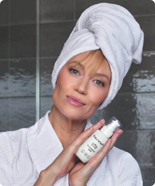 Vrouw met een handdoek op haar hoofd presenteert een flesje hannah Cleansing Milk.