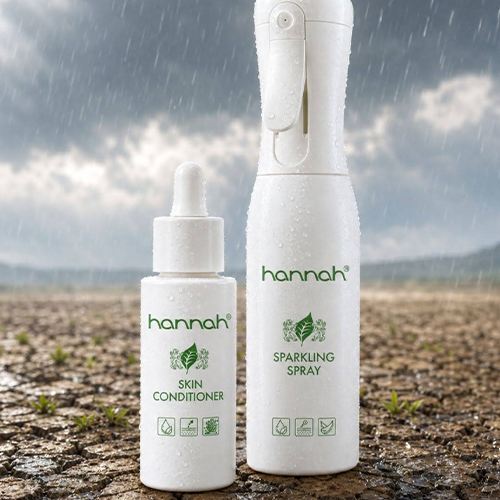Een close up van de hannah skin conditioner en de hannah sparkling spray met waterdruppels erop. Ze staan op uitgedroogde aarde tegen een regenachtige achtergrond die een droge huid symboliseert.