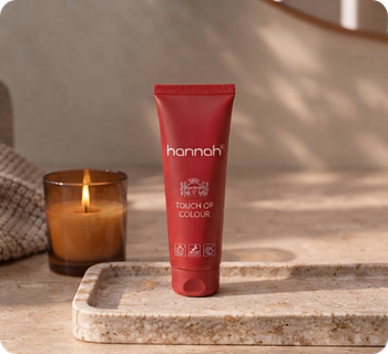 Een rode tube van hannah Touch of Colour staat rechtop op een beige marmeren plateau in een sfeervolle badkamer met een brandende kaars ernaast