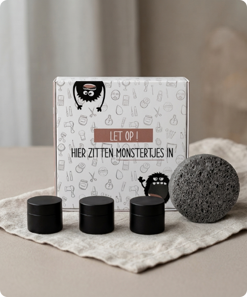 Een hannah sample set doosje met de tekst Let op hier zitten monstertjes in, omringd door drie zwarte potjes en een ronde spons.