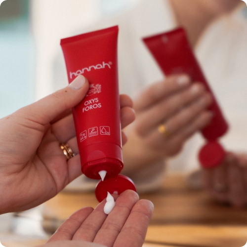 Een persoon knijpt een witte crème uit een rode Hannah Oxys Foros tube op de palm van een hand. achtergrond wazig