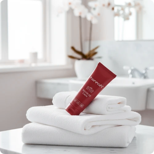 Een rode tube hannah Touch of Calm rustend op een stapel schone, witte handdoeken in een lichte badkameromgeving.