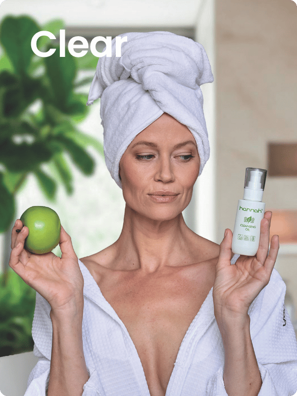 vrouw met handdoek in haar haar houdt een groene appel en een fles hannah cleansing oil vast