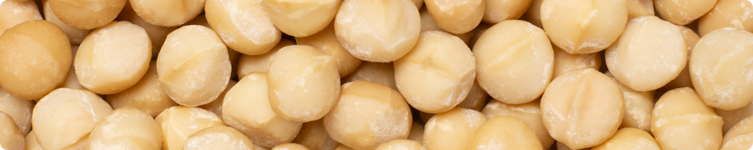 Een gedetailleerde bovenaanzicht van een grote hoeveelheid ronde, crème-witte gepelde macadamianoten die de volledige afbeelding vullen.