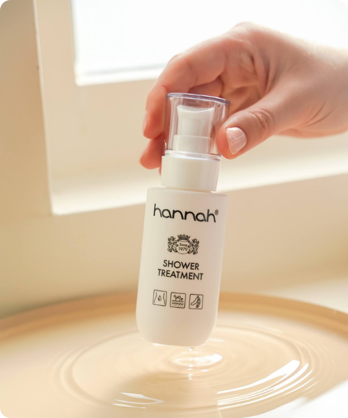 Een hand die een wit pompflasje van hannah Shower Treatment vasthoudt net boven een rimpelend wateroppervlak in een beige schaal