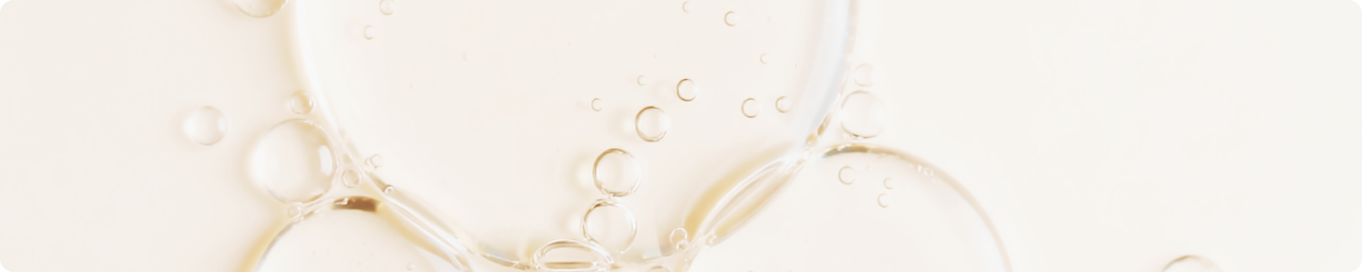 Een close-up van doorzichtige oliebellen op een gladde, beige achtergrond, wat de textuur van de siliconenolie weergeeft.