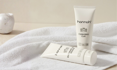 Twee tubes huidverzorgingsproducten van het merk hannah, genaamd Cleansing Clay en Enzymatic Skin Peeling, liggen op een zachte witte handdoek.