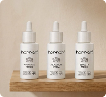 Een verticale banner met drie witte flesjes hannah serums (Opulence, Asolution, Beyouty) op een houten plankje tegen een beige muur.