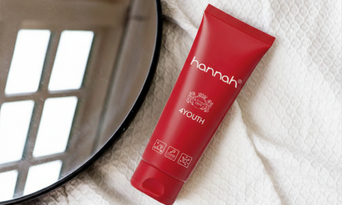 Een tube hannah 4YOUth crème geplaatst naast een ronde spiegel op een zachte, crèmekleurige ondergrond.