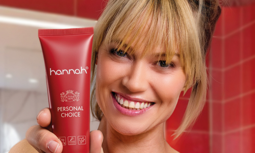 Een stralende vrouw die een tube hannah Personal Choice huidverzorgingscrème vasthoudt in een badkameromgeving.