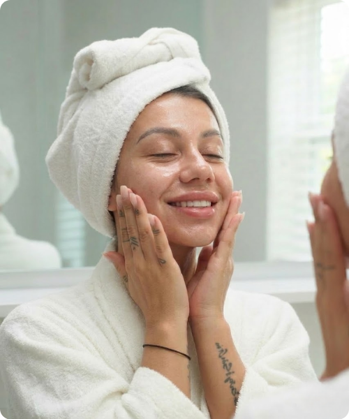 en lachende vrouw in een witte badjas en handdoek om haar hoofd, waarbij haar huid zichtbaar straalt en een gezonde glow heeft door de hannah skincare.