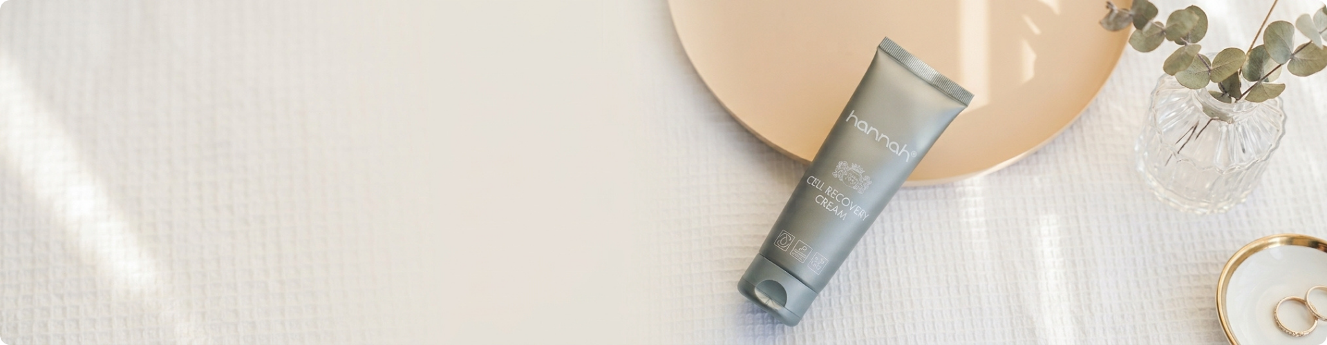hannah cell recovery cream op een witte doek naast een vaasje met takjes en sieraden