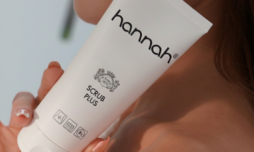 Hand houdt een tube hannah Scrub Plus vast voor een grondige lichaamsreiniging en exfoliatie van de huid.