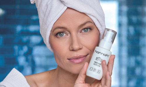 Een vrouw met een witte handdoek om haar hoofd die glimlachend het hannah Prepare Potion flesje vasthoudt.