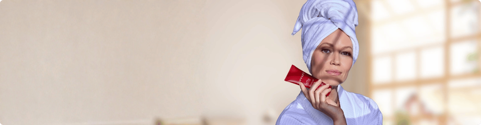 Brede banner met aan de rechterkant een vrouw in een witte badjas met een handdoek om haar hoofd die een rode hannah tube vasthoudt naast een lichte open ruimte