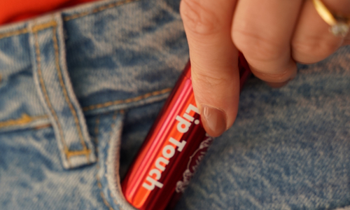 Een hand met een ring haalt een rode huls van hannah Lip Touch uit de zak van een spijkerbroek.