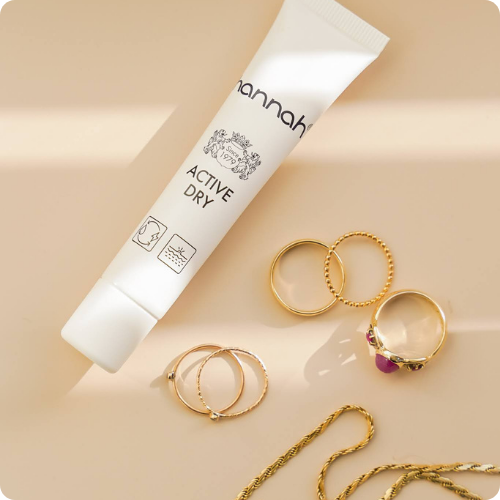 Een witte tube hannah Active Dry plat neergelegd op een beige achtergrond, omringd door gouden sieraden.