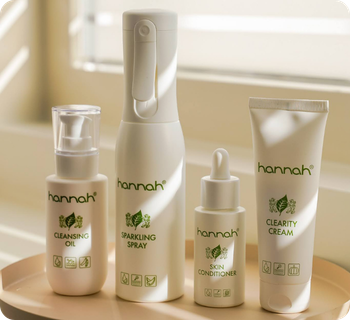 Een overzicht van vier witte hannah huidverzorgingsproducten, waaronder Cleansing Oil en Sparkling Spray, op een ronde schaal in het licht.