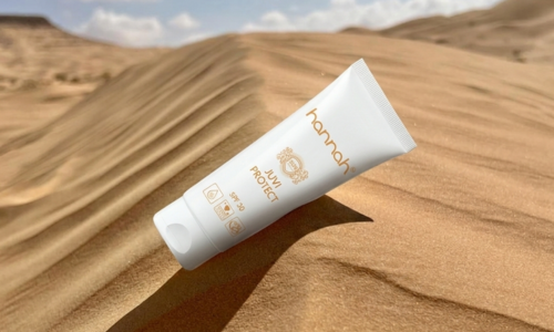 Een witte tube hannah Juvi Protect SPF30 zonnebrandcrème liggend in het zand van een zonovergoten woestijn met zandduinen op de achtergrond.