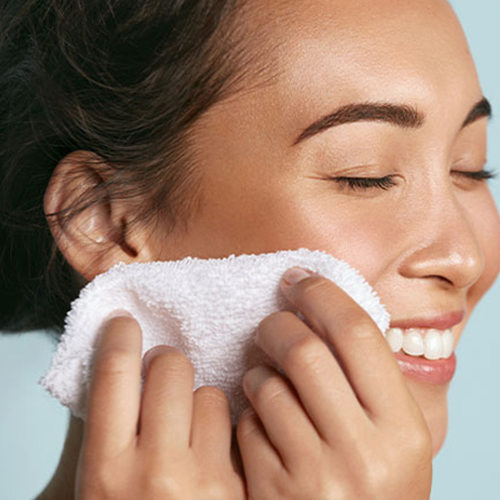Close-up van een glimlachende vrouw die haar gezicht reinigt met een zachte witte hannah kompresdoek.