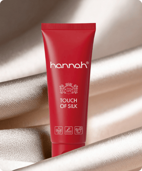 Een rode tube hannah Touch of Silk huidverzorgingsproduct geplaatst op een glanzende, champagnekleurige zijden achtergrond.