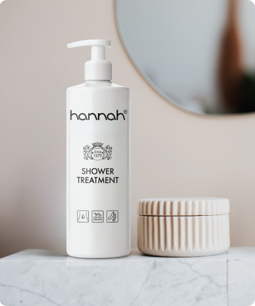 Een fles hannah Shower Treatment naast een beige pot op een marmeren ondergrond in een badkameromgeving.